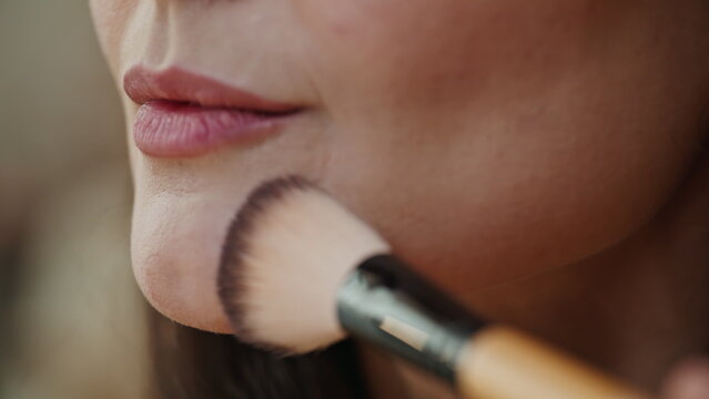 Woman brushing mineral powder on face using fluffy makeup brush closeup. 