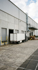 Naklejka premium White box truck parked beside a concrete warehouse wall and loading dock entrance in an industrial yard in an industrial logistics warehouse