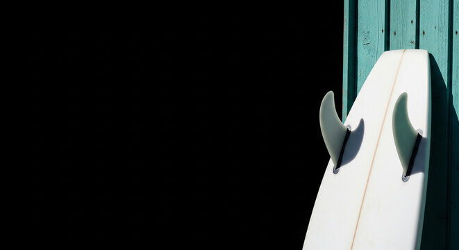 White surfboard with fins leaning against a teal wooden wall, a minimalist summer sports accessory for beach and ocean activities, evoking a relaxed coastal lifestyle.