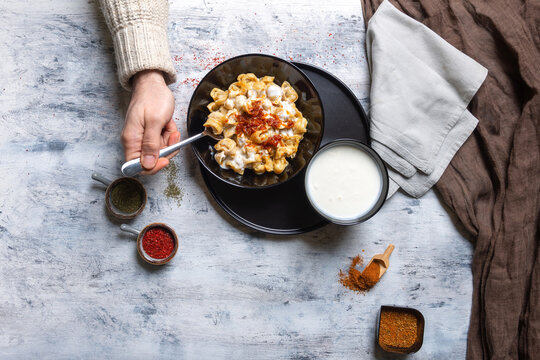 Top-Down View of Person Eating Turkish Manti Dumplings with Spices and Yogurt