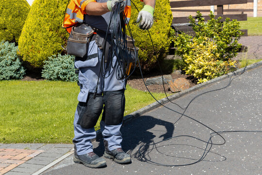 Telecoms engineer measuring and coiling fibre drop cable on driveway