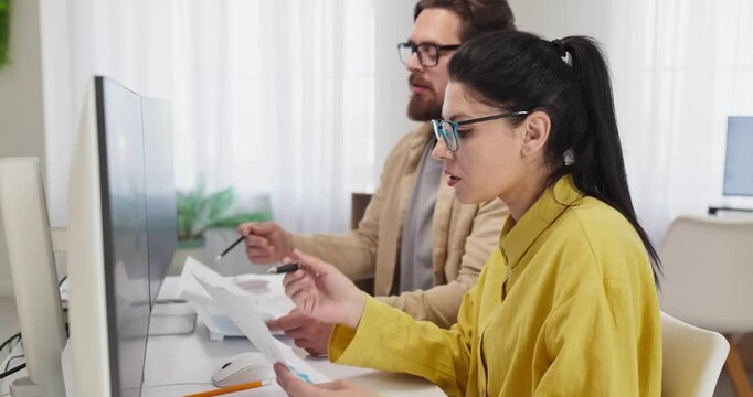 Coworkers accountants analysts do office computer analysis budgeting. Female colleague reviews paperwork while teammate checks data, confirming budgets. Concept highlights finance teamwork reports
