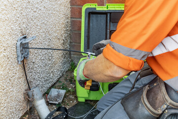 Telecoms engineer cutting fibre optic drop cable to length at exterior wall entry bracket © Tosh Lubek