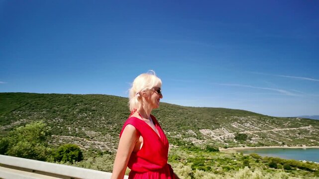 SLOW-MOTION: Woman standing on a hill overlooking the Kvarner Gulf, admiring the picturesque coastal town of Cres and its marina under a clear blue sky on a sunny summer day of Cres Island in Croatia