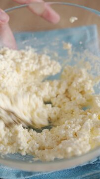 Mixing cottage cheese mixture for homemade syrniki in glass bowl with spoon. Concept of breakfast recipe and simple home cooking