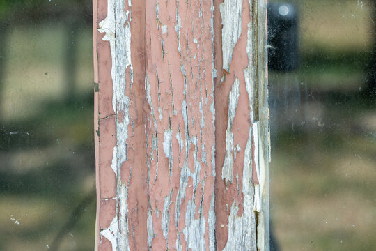 Close-up of peeling paint on a weathered wooden window frame, revealing cracked paint and aged timber. Ideal as a distressed texture or rustic background.