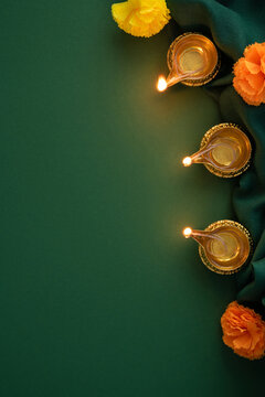 Happy Diwali with lit diyas, marigold flowers and green fabric vertical background for Indian festival