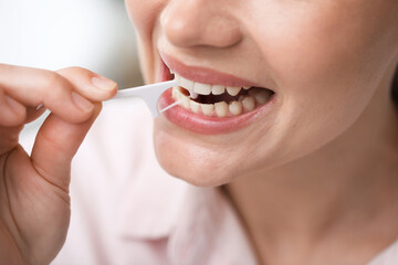 Naklejka premium Woman cleaning her teeth with dental tooth pick indoors, closeup