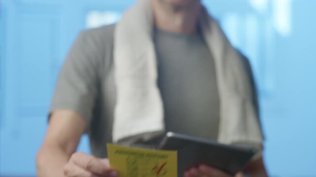 Young athletic man with a towel around his neck sticking a positive progress report on a glass surface, symbolizing successful training achievement and physical improvement after a workout