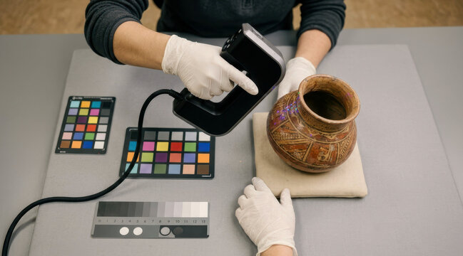Gloved museum conservator using handheld 3d scanner beside ceramic artifact in digital imaging studio