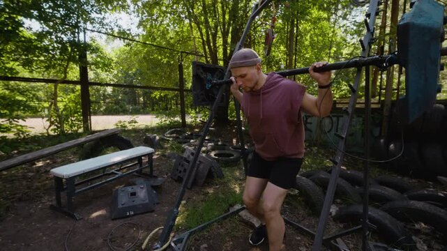 Young adult Caucasian man performing squats with homemade barbell in outdoor gym. Clip suitable for fitness marketing, strength training ads, and active lifestyle content