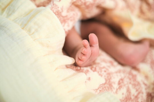 A newborn baby rests under soft pastel blankets, with tiny toes in sharp focus against a blurred face. The image reflects infant care, fragile life, family tenderness, and early parenthood.