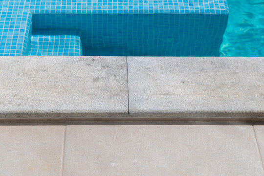 Close-up view of a modern swimming pool edge with blue tiled steps and water