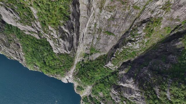 Aerial close-up of rugged granite cliffs and greenery above Lysefjord near Preikestolen, Norway, captured in summer.