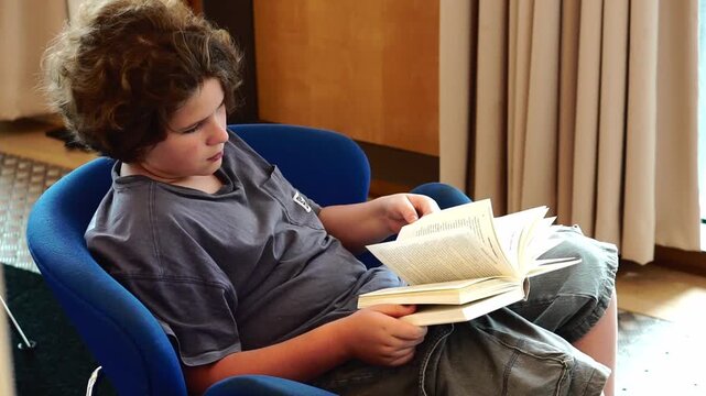 Teen boy reading book in cozy blue chair