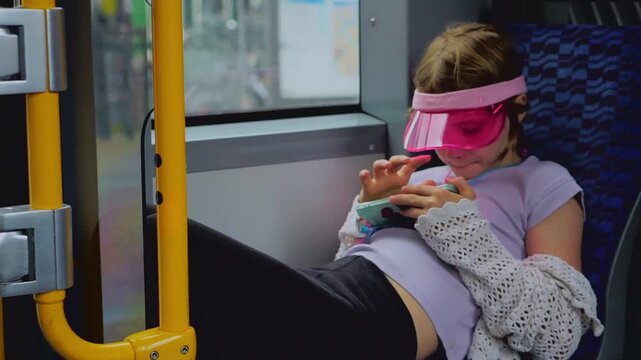 Girl in pink visor scrolling smartphone on tram with city view