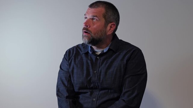 Middle aged adult man worried, concerned, anxious on gray background - Stressed worker feeling overwhelmed representing workplace burnout and crisis