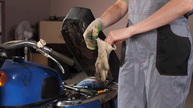 Mechanic wearing protective work gloves and overalls while preparing to repair a vintage motorcycle in a workshop, focusing on maintenance and restoration of the vehicle