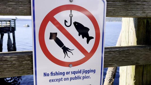 Warning sign prohibits fishing and squid jigging on a public pier. Waterfront safety notice for restricted outdoor recreation area.