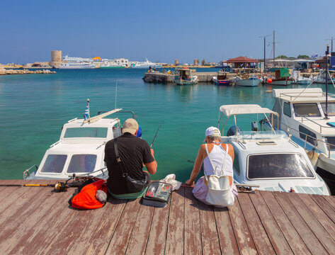 People Fishing from Harbor Pier with Boats in Mandraki Port, Rhodes, Greece