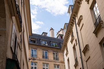 Classic residential apartment buildings line a narrow street in Paris, France. The low angle highlights traditional French architecture, balconies, and mansard roofs. © dsbedarieva