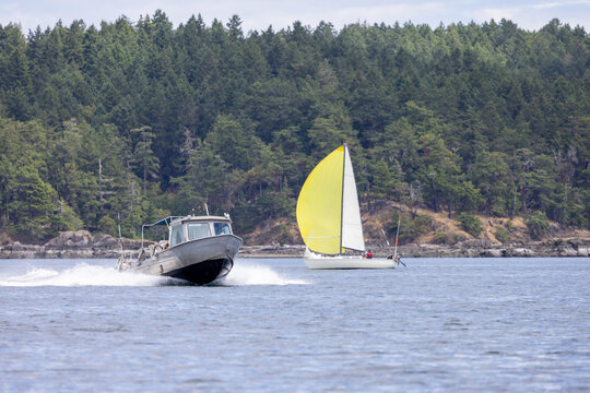 Sailboat With Yellow Spinnaker and Motorboat Passing Along Forested Coastline Near Sidney, Vancouver Island