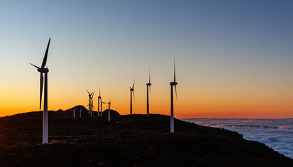 Obraz premium Wind turbines at sunset on a hillside in Bica da Cana. The wind farm generates renewable energy. Scenic view of the coastline and ocean. Located on the island of Madeira in Portugal.