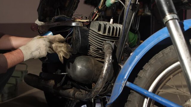 Hands in work gloves diagnosing and fixing an outdated motorcycle engine, performing maintenance and repair work on the mechanical components