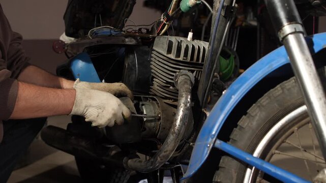 Mechanic is using a screwdriver to fix a vintage motorcycle engine, working on a complex and old motor, performing maintenance and repair