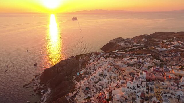 Panoramic drone footage of vibrant golden sunset over Aegean Sea with Oia cliffside village Santorini Greece