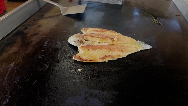 single fish cooking on hot flat top grill in restaurant kitchen