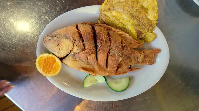hand squeezing orange slice over traditional fried tilapia fish and patacones