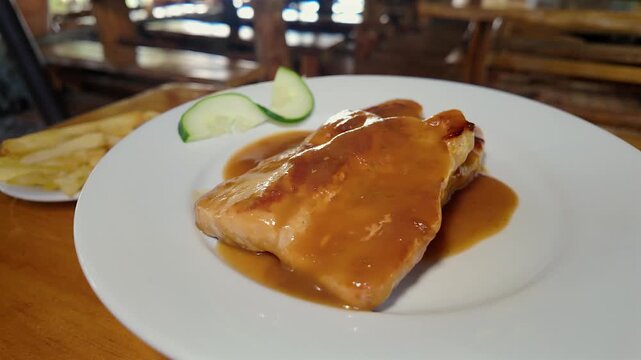 grilled pork fillets with savory bitter sweet gravy and cucumber slices on white plate