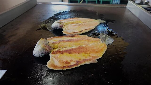 fish cooking on hot flat top grill in restaurant kitchen