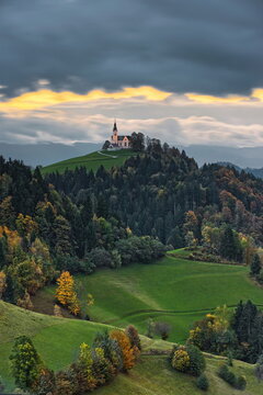 Illuminated, hilltop St.Leonard parish church seen NW-to-SE in a colorful cloudy sunrise, in the pre-Alpine Polhov Gradec hills. Crni Vrh-Slovenia-181