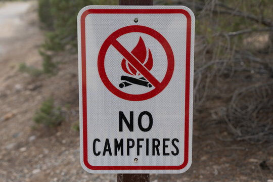 "NO CAMPFIRES" sign featuring a crossed-out flame symbol is mounted on a wooden post, warning visitors against open fires.