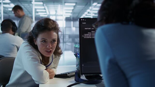 Happy technician chatting with colleague while performing maintenance on AI systems from a secondary camera angle as showing secure storage, threat prevention and cybersecurity monitoring.