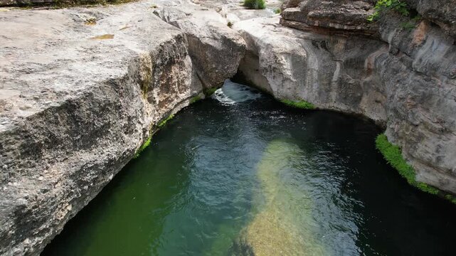 Backward reveal aerial shot of Charca del Molino (natural limestone pool) on sunny day. Arnes, Tarragona, Spain.