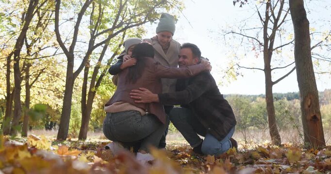 Family with children in autumn park hugging outdoors. Parents embrace happy kids amid crunchy leaves, enjoying a relaxed walk and play together in nature. Love, care and togetherness concept.