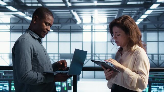 Inside a server farm, software developers work through firewall security using laptop and tablet, with security audit and risk assessment guiding the task.