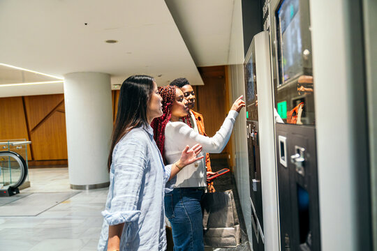 Female friend choosing snack at vending machine in mall