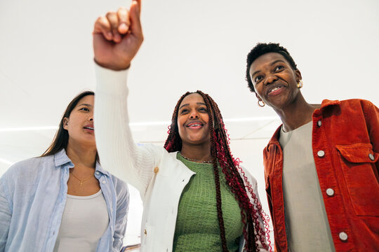 Diverse female friend group smiling and pointing indoors