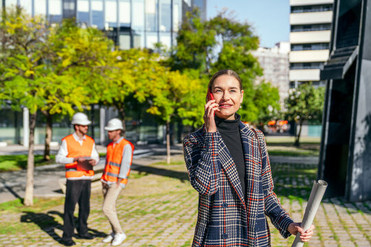 Businesswoman on phone with blueprint outside office building