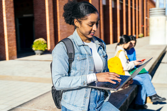Student using laptop outdoors on university campus walkway
