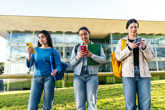 University students using smartphone on modern campus lawn