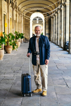 Elderly man enjoying travel with suitcase in city