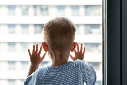 Caucasian boy looking out window with hands on glass