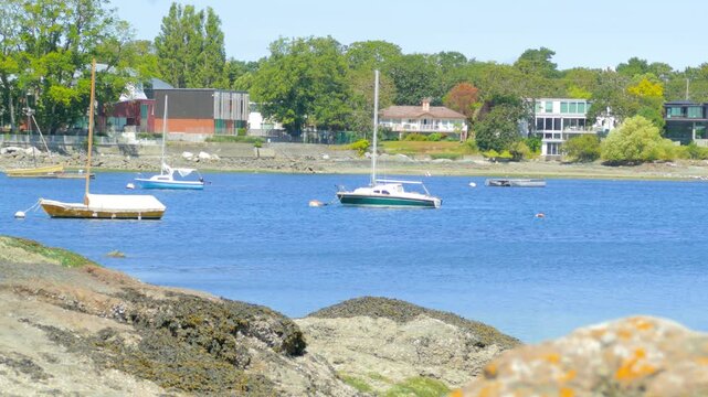 Recreational sailboats anchored in calm ocean bay by rocky shore