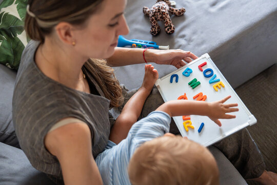 Mother and son playing alphabet letters on sofa at home