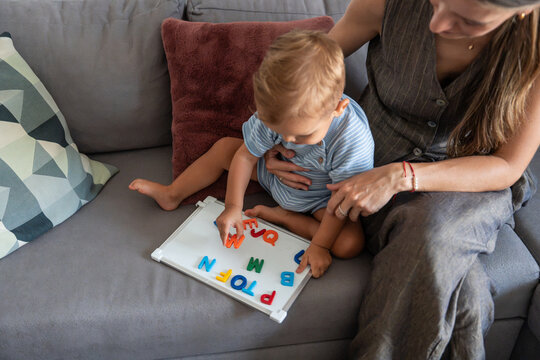 Mother and son learning letters with magnets on sofa